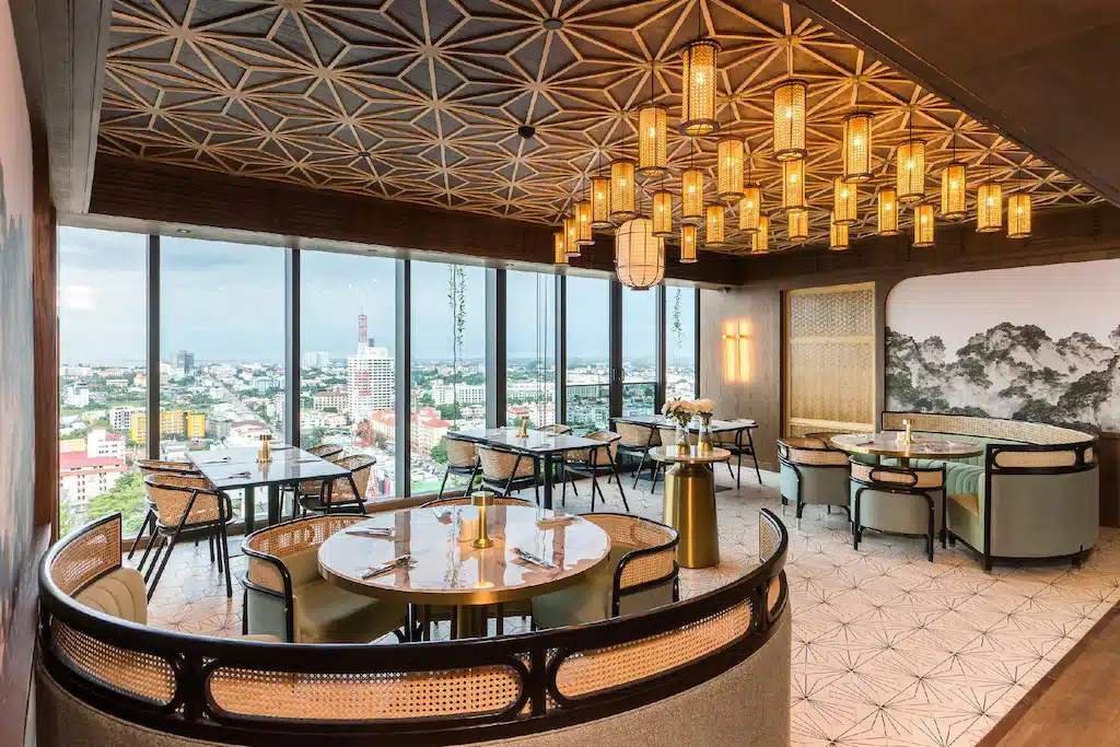 ร้านอาหารสมัยใหม่ภายในตกแต่งด้วยโต๊ะกลม เก้าอี้สไตล์ทันสมัย โคมไฟเพดานประดับตกแต่ง หน้าต่างบานใหญ่เปิดรับวิวเมือง และพื้นกระเบื้องลวดลายสวยงาม—เหมาะสำหรับผู้ที่ต้องการ พักพัทยาติดทะเล ในบรรยากาศหรูหราอย่างมีระดับ.