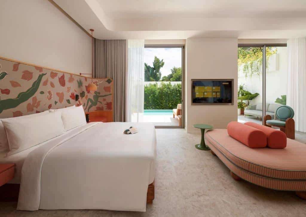 ห้องพักโรงแรมสมัยใหม่พร้อมเตียงขนาดใหญ่ หัวเตียงลายสวย เฟอร์นิเจอร์ทันสมัย ทีวีจอแบน และประตูกระจกที่เปิดออกสู่ระเบียงส่วนตัวพร้อมสระว่ายน้ำและพื้นที่สีเขียว—เหมาะสำหรับการพักผ่อนที่พัทยาติดทะเลอย่างสะดวกสบายและมีสไตล์.