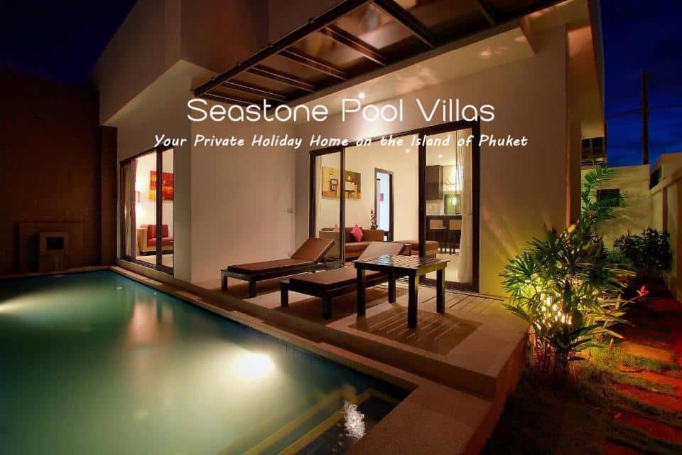 วิวยามค่ำคืนของ Seastone Pool Villas ซึ่งเป็นสถานที่ภูเก็ตในเมือง  ที่พักภูเก็ตในเมือง แสดงให้เห็นสระว่ายน้ำส่วนตัวที่มีแสงสว่าง เก้าอี้อาบแดด และวิลล่าทันสมัยพร้อมประตูลานบ้านแบบเปิด วิลล่าที่มีแสงสว่างเพียงพอสร้างบรรยากาศที่อบอุ่นและน่าดึงดูดใจ