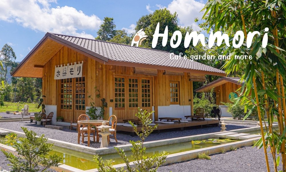 วิวกลางแจ้งของ Hommori คาเฟ่และสวนทรงเสน่ห์พร้อมอาคารไม้ที่ราย ท่องเที่ยวในภูเก็ต ล้อมไปด้วยแมกไม้เขียวขจี เหมาะสำหรับผู้ที่มองหาที่เที่ยวในภูเก็ต มีโต๊ะและเก้าอี้ตั้งอยู่ด้านนอกร้านกาแฟ