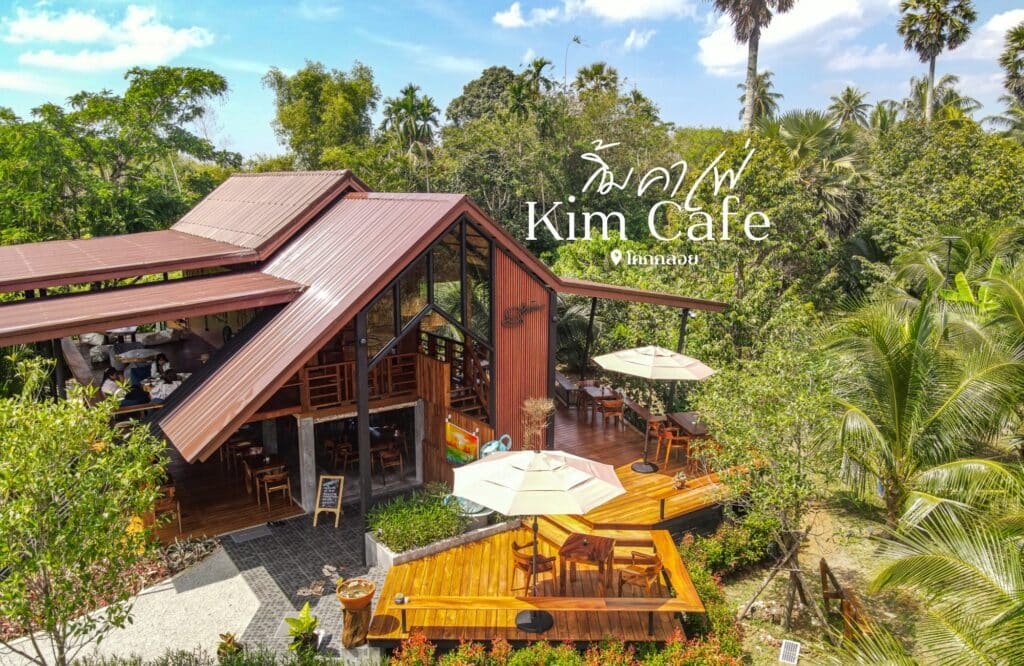 วิวทางอากาศของ Kim Cafe โครงสร้างไม้ 2 ชั้นพร้อมที่นั่งกลางแจ้ง ล้อมรอบด้วยแมกไม้เขียวขจีและต้นปาล์มในวันที่อากาศแจ่มใส ที่เที่ยวพังงา เหมาะสำหรับผู้ที่สำรวจพื้นที่พังงา