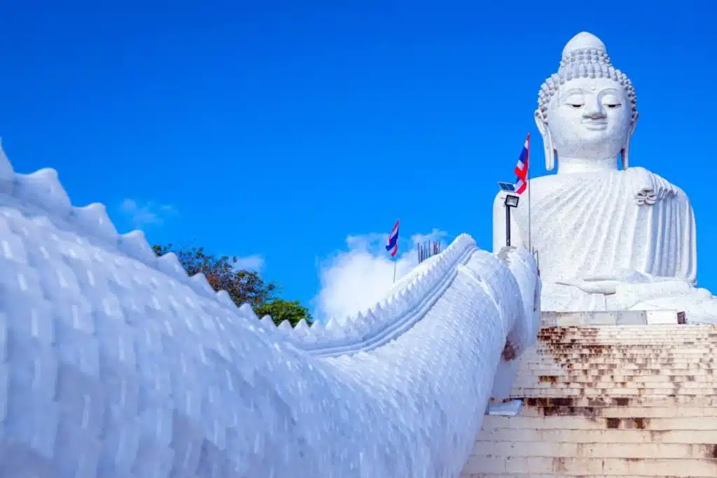 พระพุทธรูปสีขาวองค์ใหญ่ตั้งตระหง่านอยู่บนบันได สะพานสารสิน โดยมีท้องฟ้าสีฟ้าเป็นฉากหลัง ท่ามกลางราวบันไดที่ประดับประดาอย่างสวยงามและต้นไม้ทางด้านซ้าย ภาพอันเงียบสงบนี้ชวนให้นึกถึงความเงียบสงบเหนือกาลเวลาที่พบได้ใกล้กับสะพานรักสารสิน