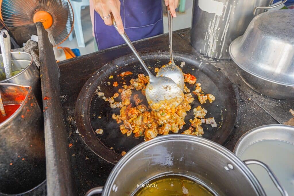 ปรุงอาหารโดย ร้านอาหารภูเก็ต ใช้อุปกรณ์ในการเตรียมอาหารบนกระทะขนาดใหญ่ล้อมรอบด้วยหม้อและกระทะต่างๆ เหมือนกับในร้านอาหารพื้นเมืองภูเก็ตที่คึกคัก