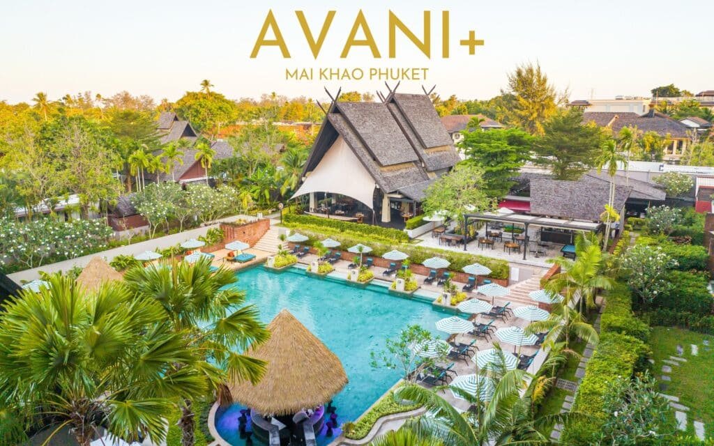 มุมมองทางอากาศของรีสอร์ท AVANI+ Mai Khao Phuket ซึ่งมีสระว่ายน้ำล้อมรอบด้วยร่มกันแดด เก้าอี้อาบแดด สวนเขียวชอุ่ม และสถาปัตยกรรมไทยดั้งเดิม โดยมี สะพา น สะพานสารสิน อันเป็นสัญลักษณ์เป็นฉากหลัง