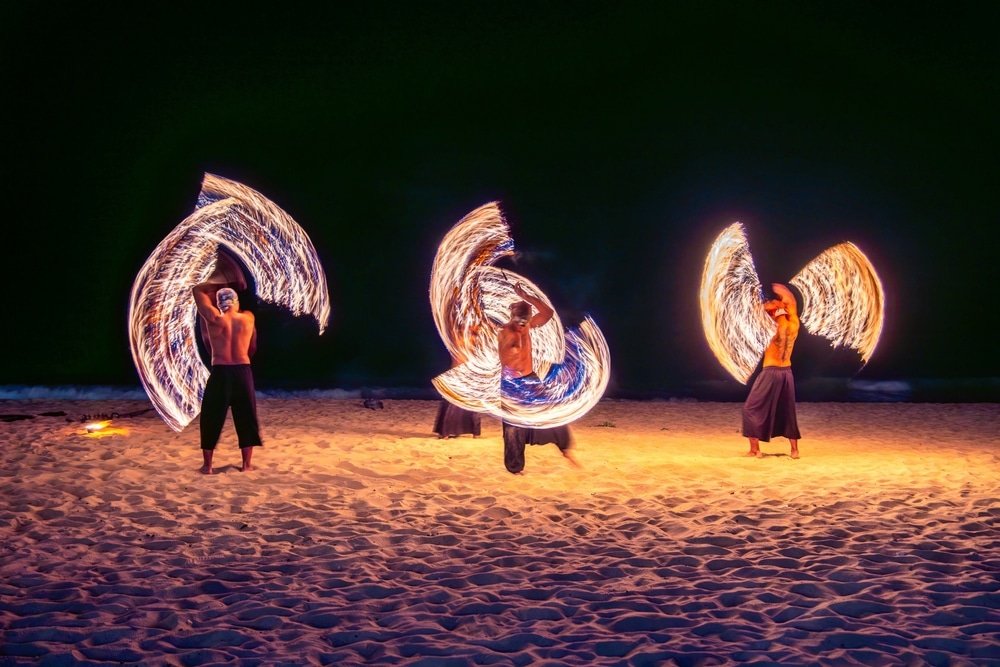 นักแสดงสามคนบนชายหาดในพังงาที่เที่ยวหมุนปอยเปลวเพลิง ทำให้เกิดแนวไฟที่น่า ที่เที่ยวพังงา หลงใหลตัดกับพื้นหลังยามค่ำคืนอันมืดมิด