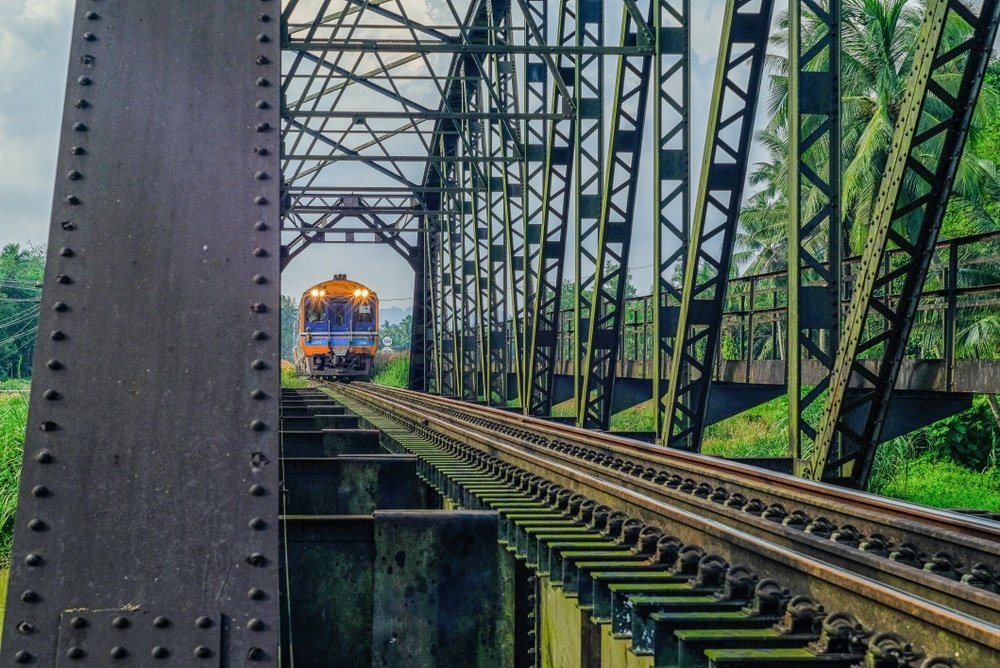 รถไฟแล่นผ่านสะพานโลหะ มีพืชพรรณเขียวชอุ่มของ ชุมพรที่เที่ยว มองเห็นได้ทั้งสองด้าน