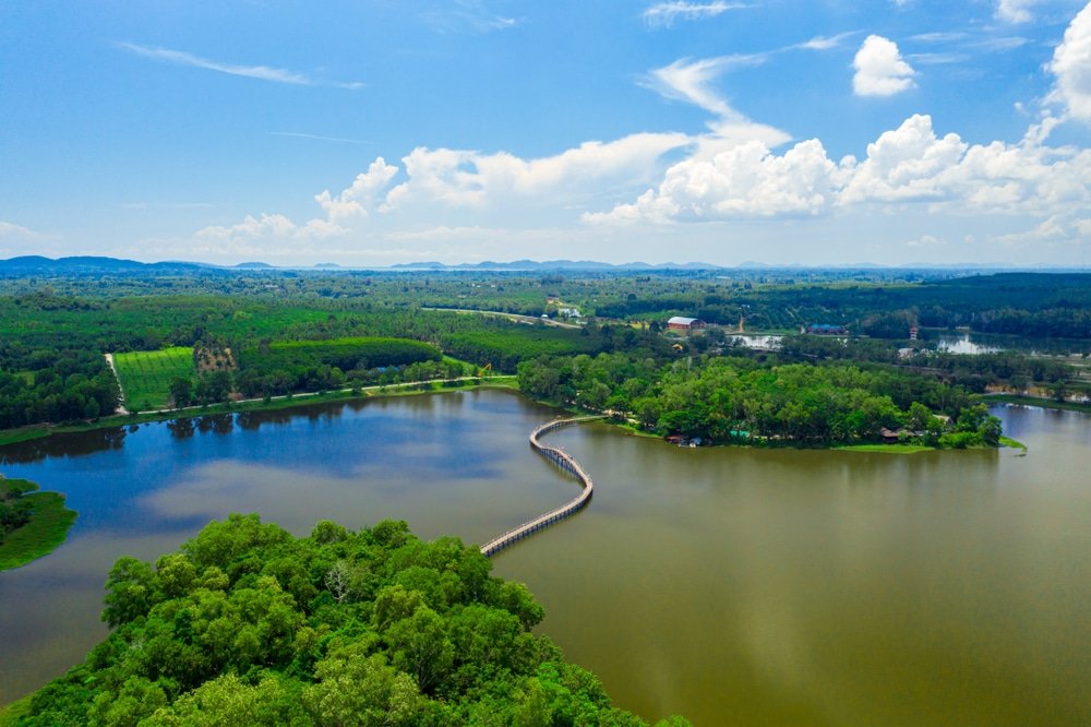 มุมมองทางอากาศของ ชุมพรที่เที่ยว พร้อมทะเลสาบที่มีสะพานยาวเชื่อมระหว่างเกาะสองเกาะที่มีป่าไม้เขียวขจีภายใต้ท้องฟ้าสีฟ้าและเมฆที่กระจัดกระจาย