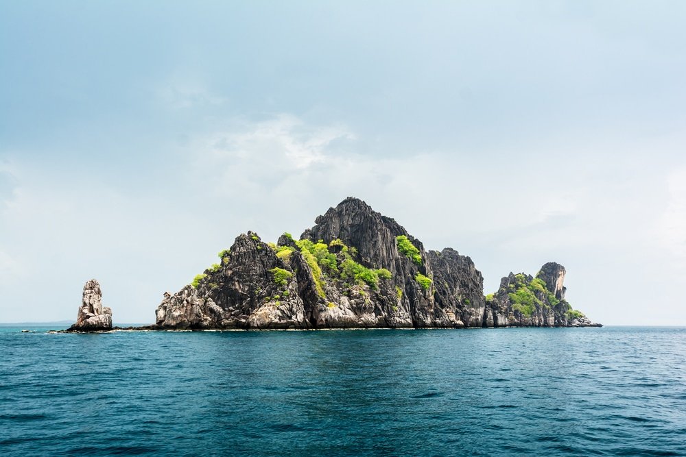 เกาะหินที่มีพืชพรรณสีเขียวกระจัดกระจายโผล่ขึ้นมาจากผืนน้ำสีฟ้าอันเงียบสงบใต้ท้องฟ้าที่มีเมฆมาก ที่เที่ยวชุมพร มอบสถานที่หลีกหนีอันเงียบสงบที่รวบรวมชุมพรที่เที่ยวไว้