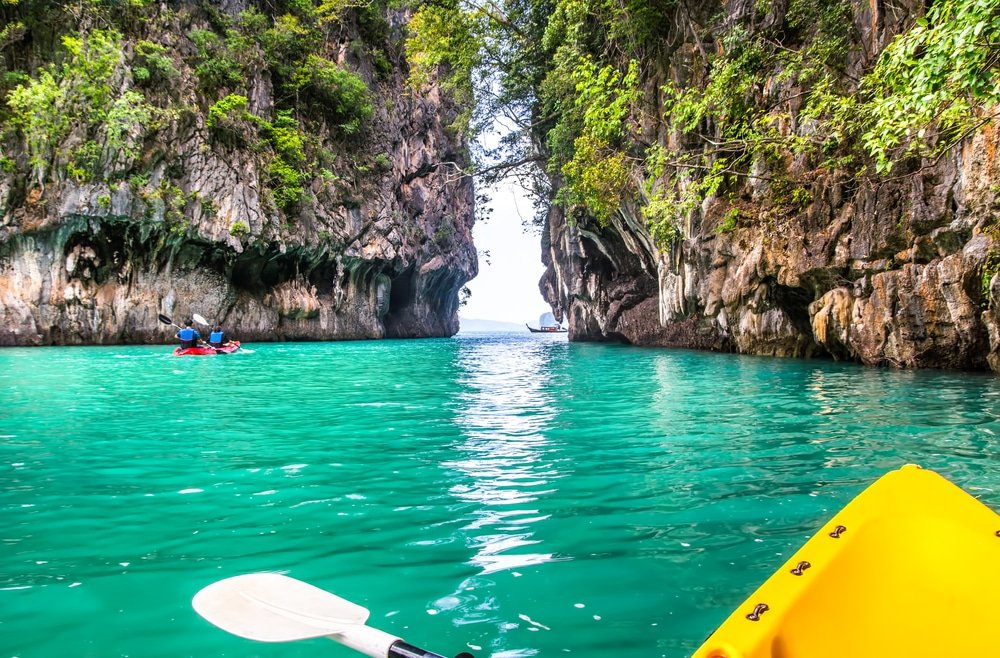 นักพายเรือคายัคพายเรือไปตาม ที่เที่ยวกระบี่ หน้าผาหินปูนสูงตระหง่านที่ปกคลุมไปด้วยพืชพรรณอันเขียวชอุ่ม ล่องไปตามผืนน้ำสีฟ้าครามใสของช่องแคบแคบที่สวยงาม ซึ่งเป็นตัวอย่างที่สมบูรณ์แบบของที่เที่ยวกระบี่