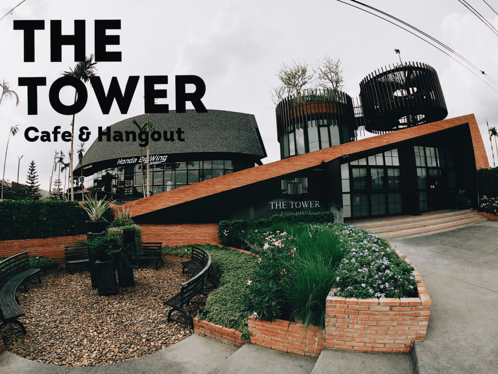 รูปภาพแสดงอาคาร The Tower Cafe & Hangout ที่มีสถาปัตยกรรมสมัยใหม่ โดยมีองค์ประกอบเป็นอิฐและกระจก ซึ่งชวนให้นึกถึงโครงสร้างที่คุณจะพบเห็นรอบๆ เกาะพีพี รายล้อมไปด้วยต้นไม้เขียวขจีและทางเดินที่น่าดึงดูด