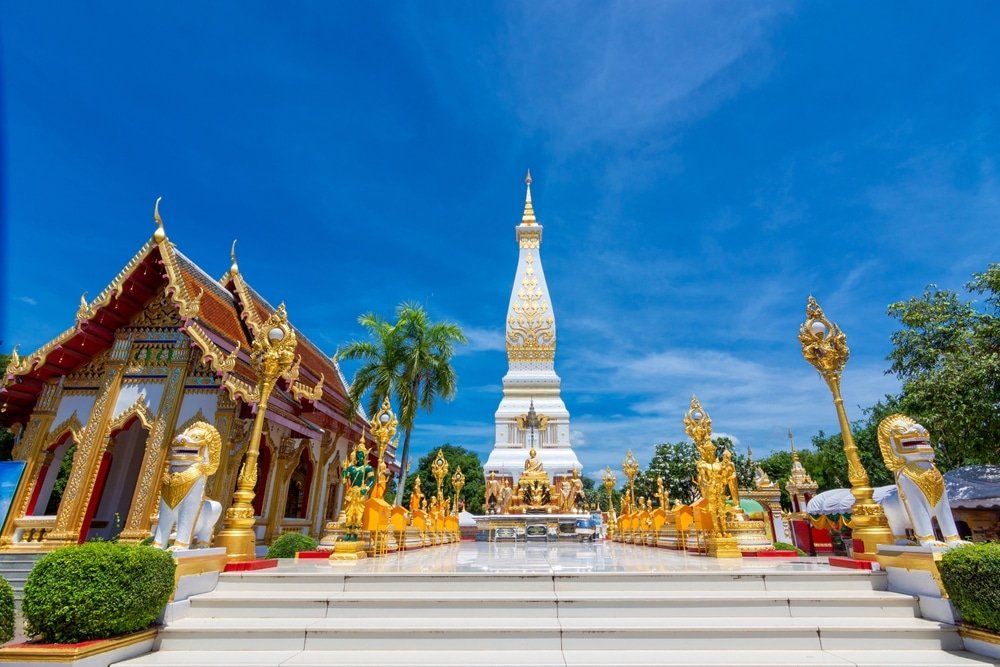 วันที่สดใสในบริเวณ ท่องเที่ยวอีสาน วัดใจกลางท่องเที่ยวอีสาน ซึ่งมีเจดีย์สูงสีขาวและสีทอง อาคารหรูหรา และรูปปั้นสิงโตที่ตั้งอยู่ท่ามกลางท้องฟ้าสีครามสดใสและความเขียวขจี.