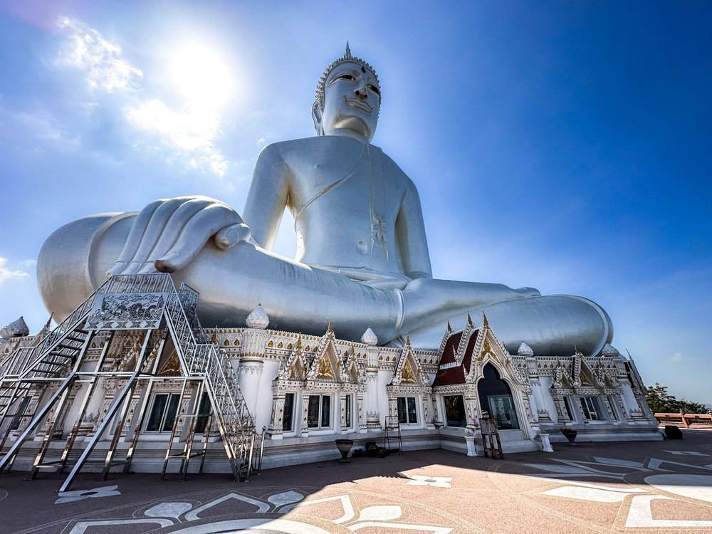 พระพุทธรูปสีขาวองค์ใหญ่ประทับอยู่บนฐานอันวิจิตรงดงามภายใต้ท้องฟ้าสี ที่เที่ยวประเทศไทย ครามสดใส มอบทัศนียภาพอันเงียบสงบแก่ผู้ที่สำรวจสถานที่เที่ยวประเทศไทย