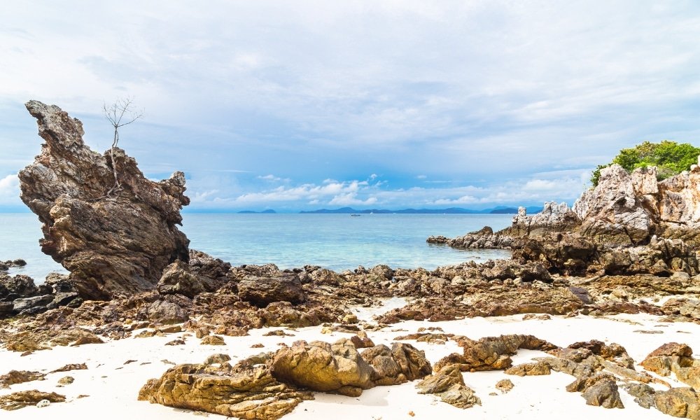 ชายหาดหินที่ “ เที่ยวระยอง ” ที่เป็นที่นิยม มีหินก้อนใหญ่กระจัดกระจาย น้ำทะเลใส และท้องฟ้าสีฟ้าครึ้ม มีหินก้อนใหญ่ตั้งตระหง่านอยู่ทางด้านซ้าย และมีเกาะต่างๆ อยู่ไกลออกไปบนขอบฟ้า.