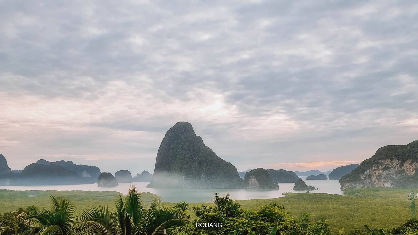 ทัศนียภาพอันสวยงามของ ที่พักเสม็ดนางชี ภูมิประเทศสีเขียวขจีพร้อมหน้าผาหินปูนสูงตระหง่าน และผืนน้ำอันเงียบสงบภายใต้ท้องฟ้าเมฆครึ้ม เหมาะอย่างยิ่งสำหรับผู้แสวงหาความสงบที่ที่พักเสม็ดนางชี.