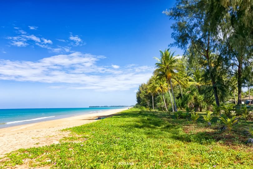 หาดทรายทอดยาวเลียบน้ำทะเลสีฟ้าคราม ล้อมรอบด้วยต้นปาล์มและความเขียวขจีภายใต้ท้องฟ้าสีฟ้าใส ซึ่งเป็นฉากสำคัญที่เที่ยวเขาหลัก.