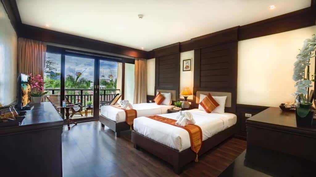 ห้องพักในโรงแรม ที่พักอ่าวนาง ที่มีเตียงเดี่ยว 2 เตียง เฟอร์นิเจอร์ไม้สีเข้ม โต๊ะทำงาน และระเบียงพร้อมประตูกระจกที่มองเห็นความเขียวขจี เหมาะสำหรับนักเดินทางที่กำลังมองหาอ่าวนางกระบี่ในบรรยากาศที่เงียบสงบและสวยงาม.