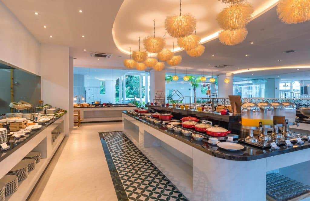 ร้านอาหารบุฟเฟ่ต์ทันสมัยพร้อมแผงอาหาร อาหาร และน้ำผลไม้ต่างๆ จัดเรียงบนเคาน์เตอร์หินอ่อนใต้โคมไฟ ที่พักอ่าวนาง ระย้าตกแต่ง เหมาะสำหรับแขกที่มาพักที่กระบี่อ่าวนางที่กำลังมองหาประสบการณ์การรับประทานอาหารที่มีสไตล์ในบริเวณใกล้เคียง.