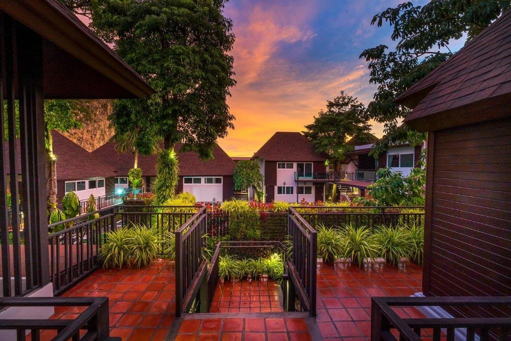 วิวของลานสวนยามพระอาทิตย์ตกดิน พร้อมด้วยพื้นกระเบื้องสีแดง ต้นไม้เขียวชอุ่ม และอาคารแบบบ้าน เหมาะสำหรับการพักผ่อนที่ ที่พักอ่าวนาง ใต้ท้องฟ้าสีสันสดใส.