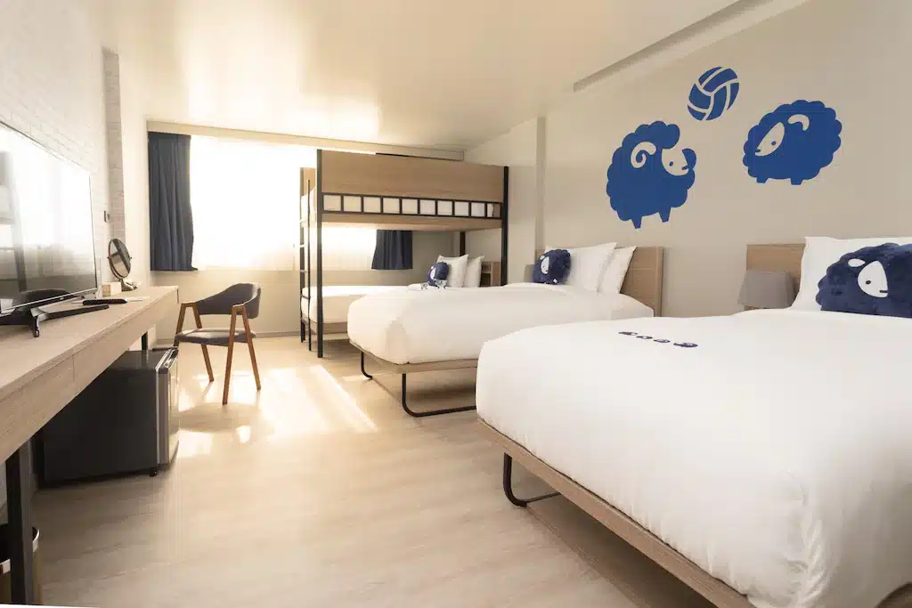 ห้องพักโรงแรมทันสมัยที่ รีสอร์ทกระบี่ พร้อมเตียงแฝด 2 เตียง เตียงสองชั้น เฟอร์นิเจอร์ไม้สไตล์มินิมอล ทีวีจอแบน และสติกเกอร์แกะสีฟ้าขี้เล่นบนผนัง.