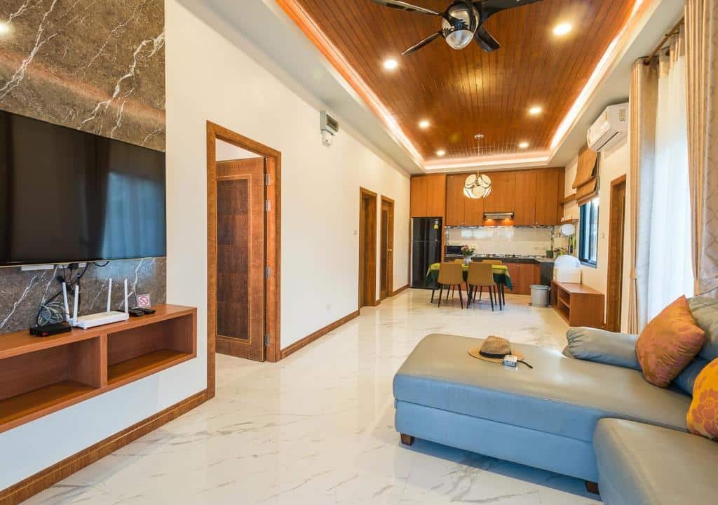 ห้องนั่งเล่นและห้องครัวแบบเปิดโล่งทันสมัยพร้อมพื้นหินอ่อน ทีวีติดผนัง ที่พักอ่าวนางราคาถูก  โซฟาสีเทา พื้นที่รับประทานอาหาร และตกแต่งด้วยไม้ เหมาะสำหรับการพักผ่อนหลังจากสำรวจหาดกระบี่อ่าวนาง หรือเพลิดเพลินกับการพักผ่อนในอ่าวนางราคาถูก.