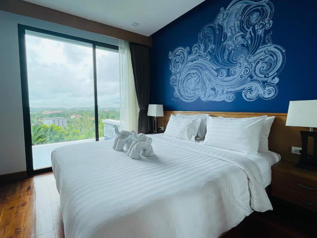 ห้องพักใน โรงแรม ที่พักอ่าวนาง  ที่มีเตียงขนาดใหญ่ ผ้าปูที่นอนสีขาว หงส์ผ้าเช็ดตัว ผนังลายคลื่นสีฟ้า โคมไฟข้างเตียง และหน้าต่างที่มองเห็นวิวเมืองและต้นไม้เขียวขจี เหมาะสำหรับการพักอย่างผ่อนคลายที่อ่าวนางกระบี่.