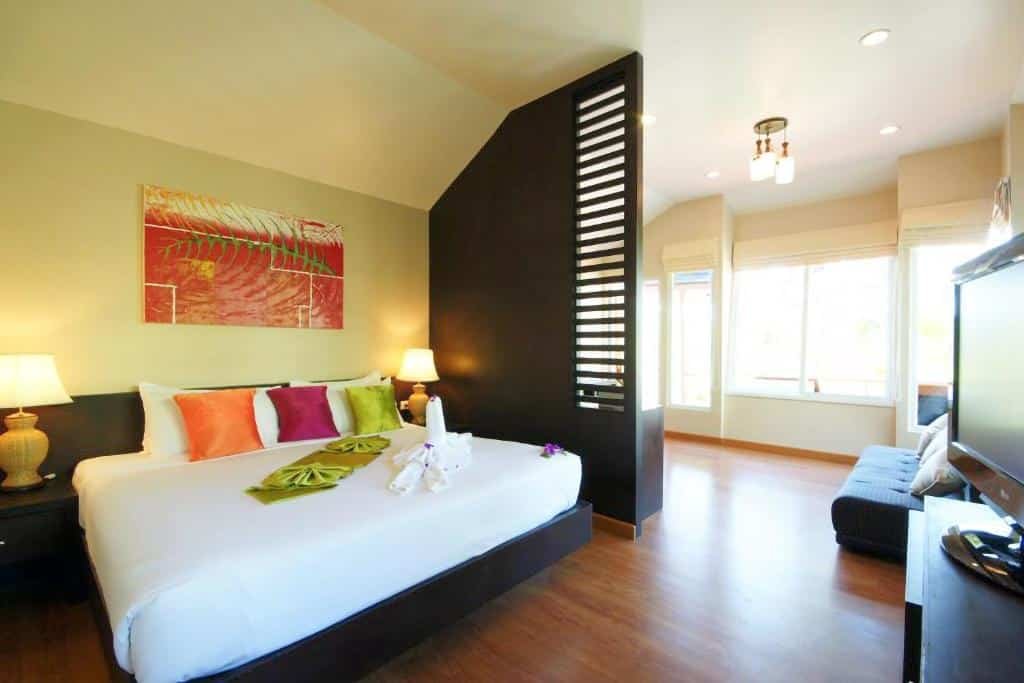 ห้องพักโรงแรมทันสมัยที่ โรงแรมกระบี่ พร้อมเตียงขนาดใหญ่ หมอนสีสันสดใส โคมไฟข้างเตียง ฉากกั้นห้องสีดำ พื้นที่นั่งเล่นแสนสบาย และหน้าต่างที่ให้แสงธรรมชาติส่องเข้ามา.