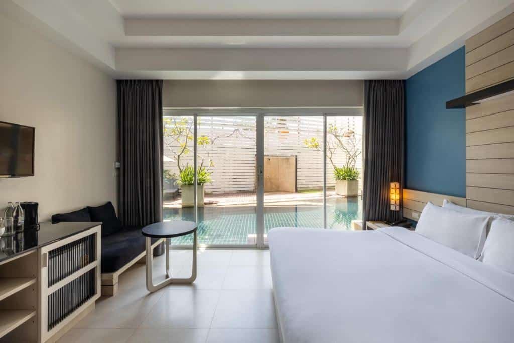ห้องพักในโรงแรมทันสมัยพร้อมเตียงขนาดใหญ่ ทีวีติดผนัง พื้นที่นั่งเล่น และประตูกระจกบานเลื่อนที่เปิดออกสู่สระว่ายน้ำส่วนตัวและลานบ้านที่มีต้นไม้อยู่ด้านนอก เหมาะสำหรับการพักผ่อน ที่พักอ่าวนางกระบี่