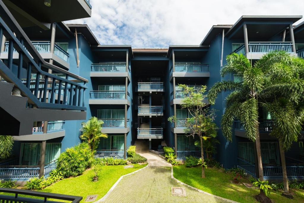 อาคารอพาร์ตเมนต์สีฟ้าทันสมัยพร้อมระเบียงหลายด้านมองเห็นลานภายในที่มีภูมิทัศน์สวยงามพร้อมต้นปาล์ม  ที่พักอ่าวนาง นำเสนออ่าวนางที่มีสไตล์ภายใต้ท้องฟ้าที่มีเมฆบางส่วน.