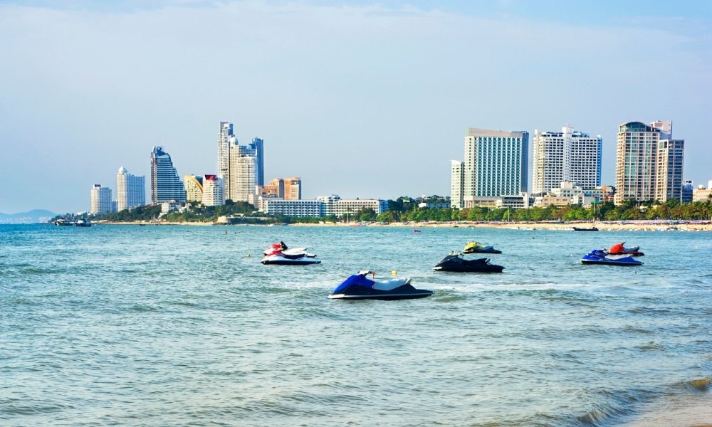 ขี่เจ็ตสกีหลายลำบนผืนน้ำใกล้ เที่ยวพัทยา ชายหาด โดยมีโรงแรมสูงทันสมัยเป็นฉากหลังภายใต้ท้องฟ้าแจ่มใส ทำให้เป็นฉากที่สมบูรณ์แบบสำหรับทุกคนที่กำลังมองหาที่เที่ยวพัทยาติดทะเลขณะสำรวจพัทยาที่เที่ยว.