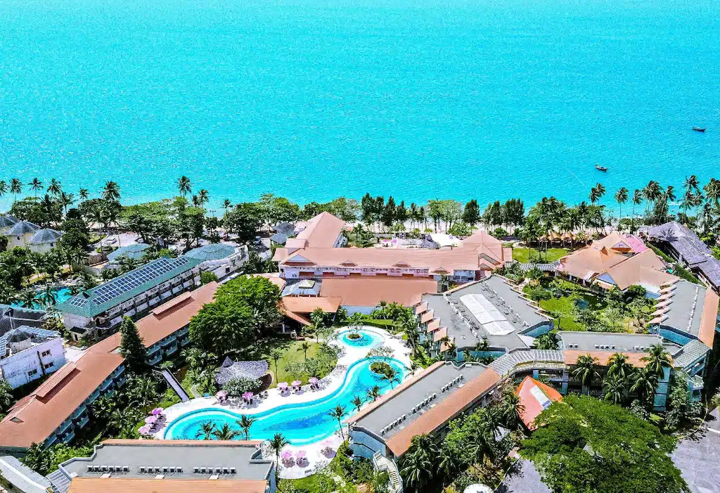 มุมมองทางอากาศของรีสอร์ทริมชายหาดขนาดใหญ่ที่ พักอ่าวนาง ซึ่งมีอาคารหลายหลัง สระว่ายน้ำคด ที่พักอ่าวนาง เคี้ยว ต้นปาล์ม และมหาสมุทรเป็นพื้นหลังภายใต้ท้องฟ้าสีฟ้าใส.