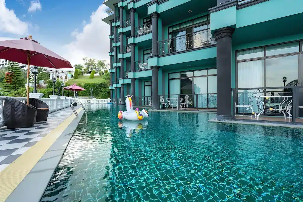 อาคาร โรงแรมกระบี่ ทันสมัยพร้อมระเบียงมองเห็นสระว่ายน้ำใสที่มียูนิคอร์นเป่าลมขนาดใหญ่ มีที่นั่งและร่มริมสระที่มองเห็นได้ เหมาะสำหรับการพักผ่อนที่รีสอร์ทกระบี่.
