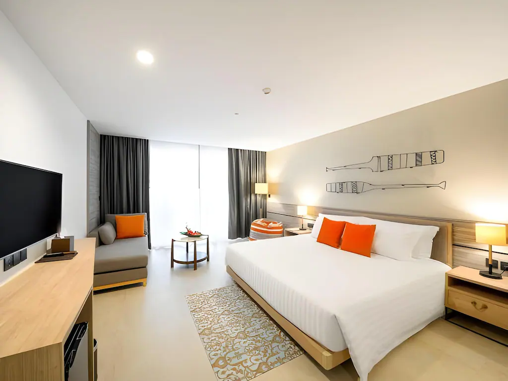 ห้องพัก ที่พักอ่าวนาง ในโรงแรมทันสมัยพร้อมเตียงคิงไซส์ หมอนสีส้ม โซฟา ทีวี โต๊ะทำงาน และหน้าต่างบานใหญ่ ศิลปะนามธรรมเหนือเตียงสร้างบรรยากาศที่มีสไตล์ เหมาะสำหรับผู้ที่มองหาอ่าวนางราคาถูกในบรรยากาศสบายๆ.