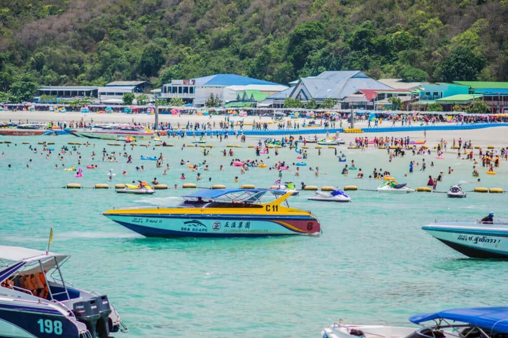 ที่เที่ยวพัทยาติดทะเลที่มีชีวิตชีวา เที่ยวพัทยา ฉากชายหาดที่พลุกพล่านนี้ทำให้ผู้คนว่ายน้ำและผ่อนคลาย ในขณะที่เรือเร็วลอยอยู่บนน้ำทะเลสีฟ้าคราม โดยมีอาคารและต้นไม้เป็นฉากหลัง เหมาะสำหรับทุกคนที่กำลังมองหาเที่ยวพัทยา.