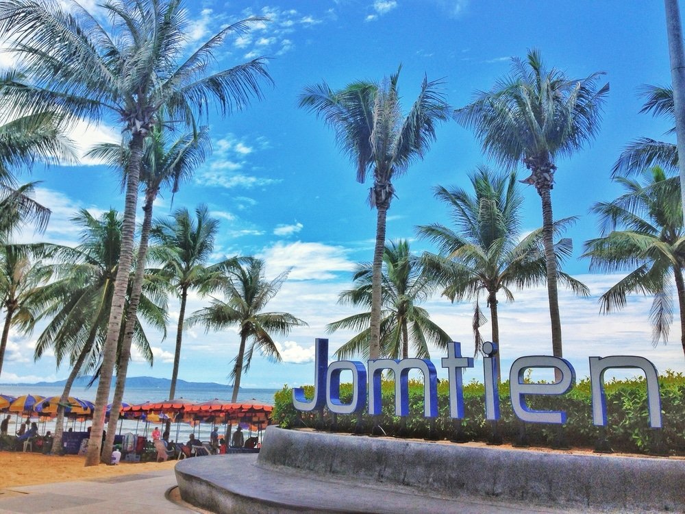 ต้นปาล์มและป้าย "จอมเทียน" ขนาดใหญ่ริมชายหาดพร้อมร่มใต้ท้องฟ้าสีคราม สัมผัสบรรยากาศของพัทยาที่เที่ยวและร้านดัง ที่เที่ยวพัทยา ติดทะเล.