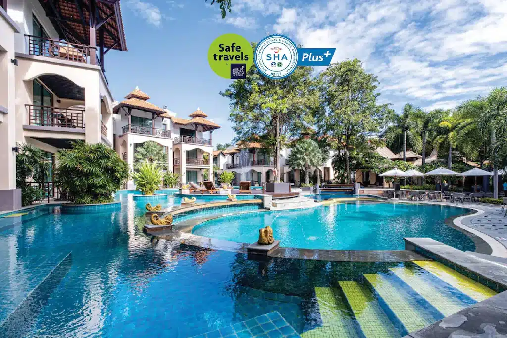 บริเวณสระว่ายน้ำกลางแจ้งที่รีสอร์ทพร้อมระเบียง พื้นที่เขียวขจี และที่นั่งเล่น โลโก้ใบรับรองความปลอดภัยจะแสดงที่ด้านบนของภาพ เหมาะสำหรับผู้ที่กำลังมองหาที่พักพัทยาราคาถูกเพื่อการพักผ่อนอย่างผ่อนคลาย.