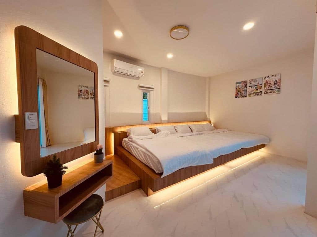 ห้องนอน ที่พักกาญจนบุรี สมัยใหม่ที่รีสอร์ทกาญจนบุรี ประกอบด้วยเตียงขนาดใหญ่ กระจกติดผนัง เก้าอี้สตูลขนาดเล็ก และไฟใต้เตียงนุ่มนวล ภาพวาดกรอบสามภาพประดับผนังด้านหลังเพื่อความอบอุ่นและสไตล์ที่ทันสมัย.