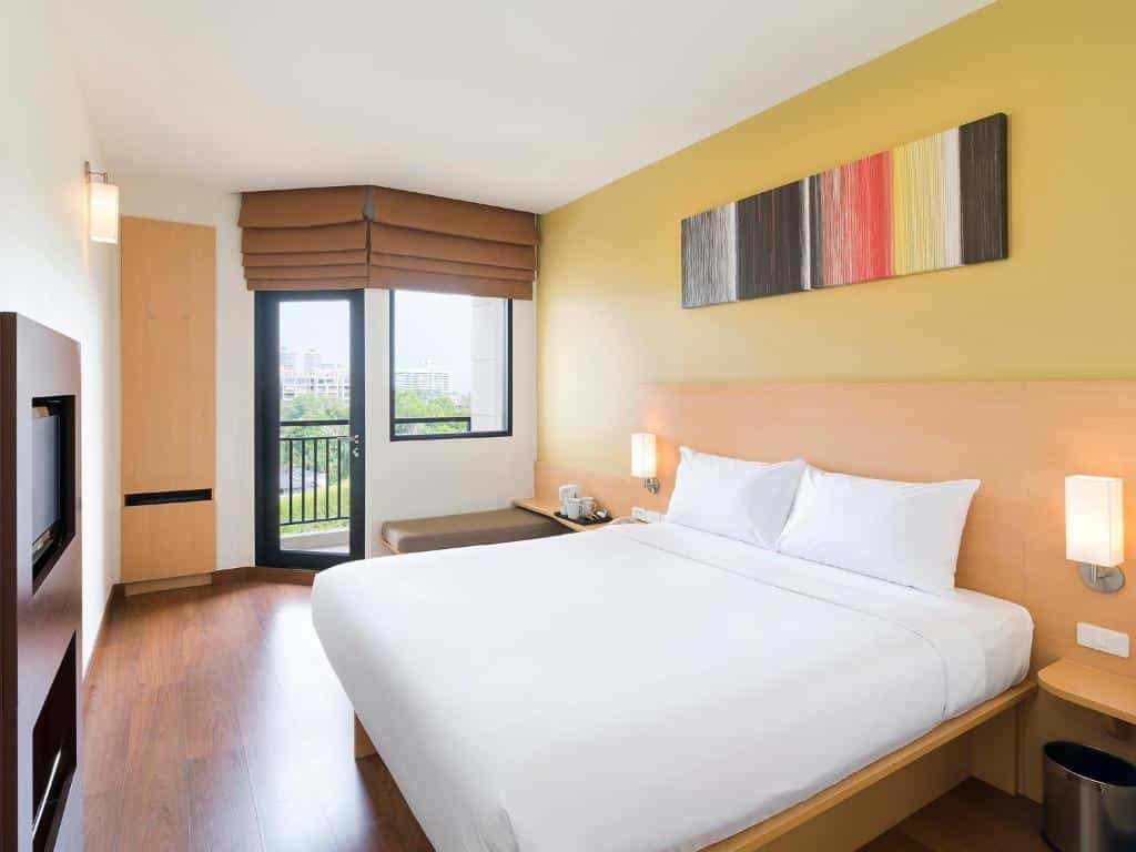 ห้องพักในโรงแรมทันสมัยพร้อมเตียงขนาดใหญ่ โคมไฟข้างเตียง ศิลปะบนฝาผนัง และหน้าต่างที่มีเฉดสีน้ำตาลมอบความสะดวกสบายและทิวทัศน์ สถานที่ท่องเที่ยวหัวหิน เมือง เหมาะสำหรับพี่น้องชาวหัวหินที่ต้องการพักผ่อนหลังจากสำรวจพื้นที่ท่องเที่ยวหัวหิน.