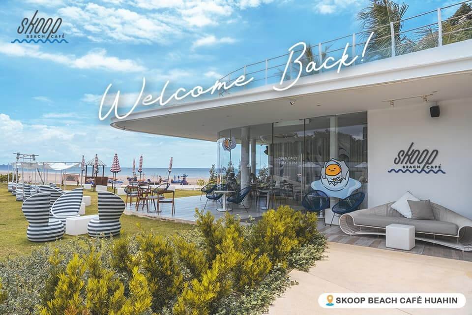 วิวกลางแจ้งของ Skoop Beach Café พร้อมที่นั่งทันสมัย ร่มชายหาด และข้อความ "Welcome Back!" text—เหมาะสำหรับการพักผ่อนกลางแดด  ท่องเที่ยวหัวหิน ณ หนึ่งในพื้นที่ท่องเที่ยวหัวหิน ท้องฟ้าสีครามและชายหาดที่สวยงามเป็นฉากหลัง.