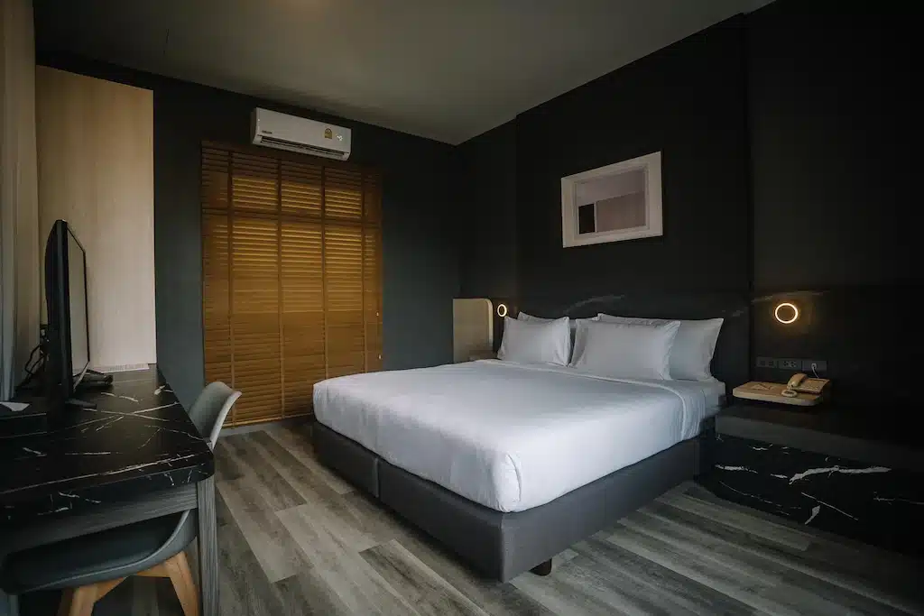 ห้องพักในโรงแรมทันสมัยพร้อมเตียงคู่ โต๊ะและเก้าอี้ ทีวีติดผนัง หน้าต่าง ท่องเที่ยวสตูล พร้อมมู่ลี่ไม้ และการตกแต่งแบบมินิมอลในโทนสีกลางๆ เหมาะสำหรับการพักผ่อนหลังจากสำรวจพื้นที่ท่องเที่ยวหัวหิน.