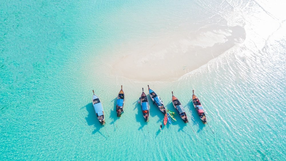 มุมมองทางอากาศของเรือไม้ 6 ลำที่ทอดสมออยู่ในน้ำทะเลสีฟ้าครามใสใกล้เกาะทรายเล็กๆ เก็บภาพความ ท่องเที่ยวสตูล งามอันเงียบสงบของที่เที่ยวธรรมชาติหัวหินสำหรับการผจญภัยใน ท่องเที่ยวหัวหิน.