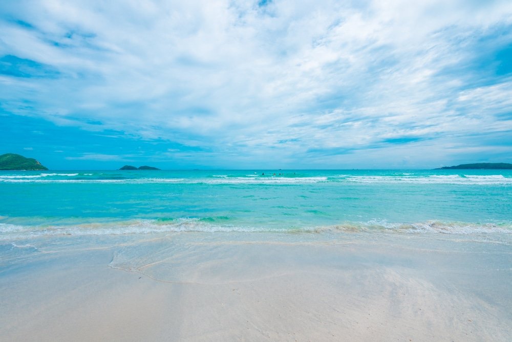 ชายหาดทรายขาวละเอียดพร้อมน้ำทะเลสีเทอร์ควอยส์ใสสะอาดใต้ ที่เที่ยวใกล้กรุงเทพ ท้องฟ้าที่มีเมฆบางส่วนปกคลุม ที่ซึ่งคลื่นเล็กๆ กลิ้งเบาๆ เข้าสู่ชายฝั่ง—เหมาะอย่างยิ่งสำหรับผู้ที่ต้องการสัมผัสประสบการณ์การท่องเที่ยวสตูลที่เงียบสงบ.