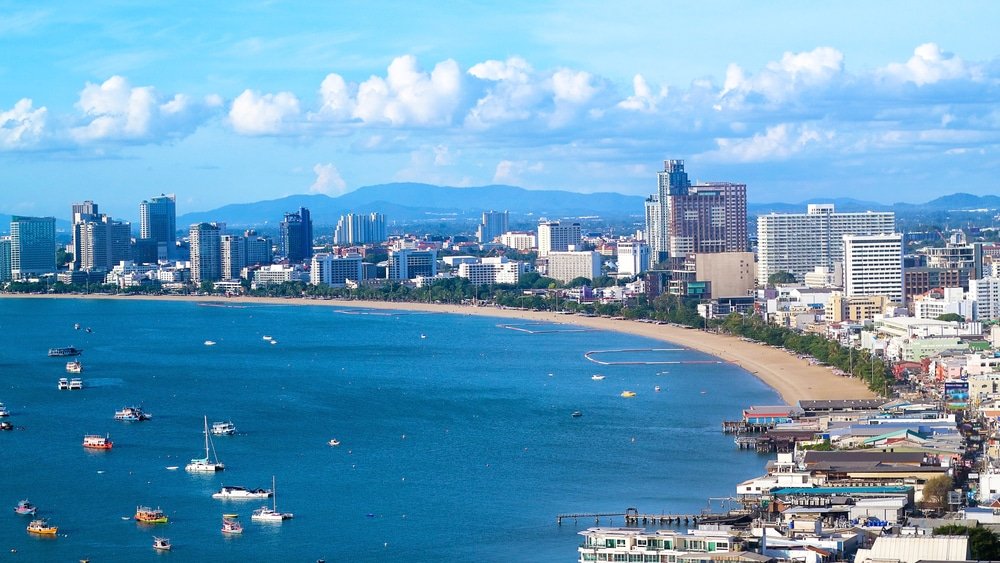 ที่เที่ยวใกล้กรุงเทพ ภาพพาโนรามาของเมืองชายฝั่งทะเล หนึ่งในสถานที่ท่องเที่ยวชั้นนำของสตูล พร้อมตึกสูงระฟ้า ชายหาดทราย และเรือที่จอดทอดสมออยู่ในน้ำสีฟ้า ภายใต้ท้องฟ้าที่มีเมฆบางส่วน.