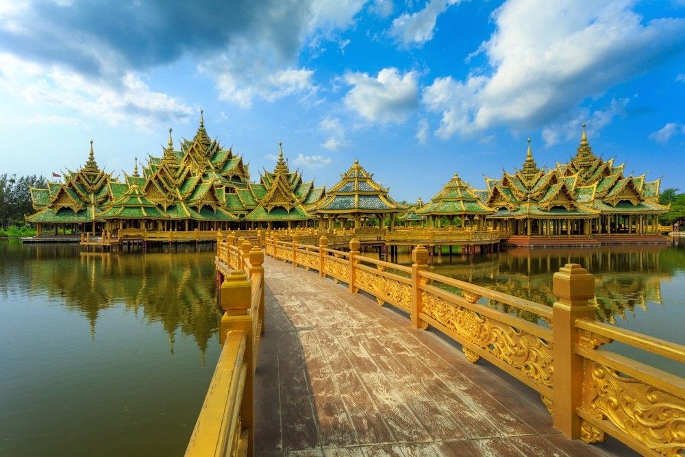 สะพานทองคำทอดยาวไปยังศาลาหลายชั้นที่ตกแต่งอย่างวิจิตรบรรจง มี ที่เที่ยวใกล้กทม หลังคาสีเขียว ล้อมรอบด้วยน้ำและท้องฟ้าสีคราม—สถานที่ท่องเที่ยวสตูลที่น่าหลงใหล เหมาะสำหรับการผจญภัยครั้งต่อไปของคุณ.