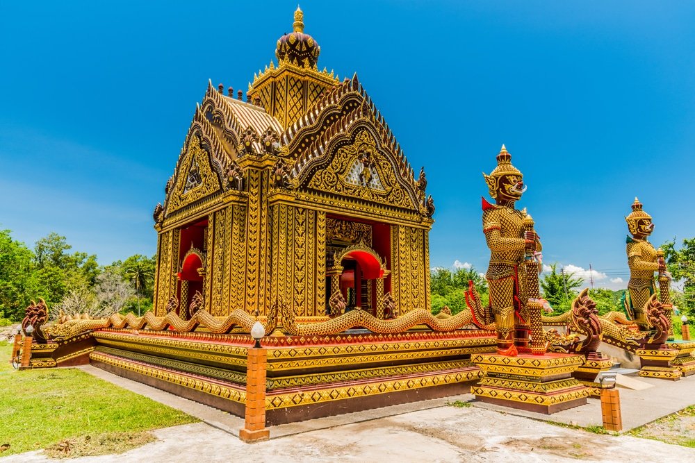 วัดไทยสีทองอลังการที่มีการ ท่องเที่ยวหัวหิน ออกแบบอันวิจิตรบรรจง ขนาบข้างด้วยรูปปั้นผู้พิทักษ์ขนาดใหญ่ 2 องค์ และต้นไม้เขียวขจีใต้ท้องฟ้าสีฟ้าใส สถานที่ท่องเที่ยวที่น่าทึ่งของหัวหินเหมาะสำหรับการเยี่ยมชมครั้งต่อไปของคุณ.