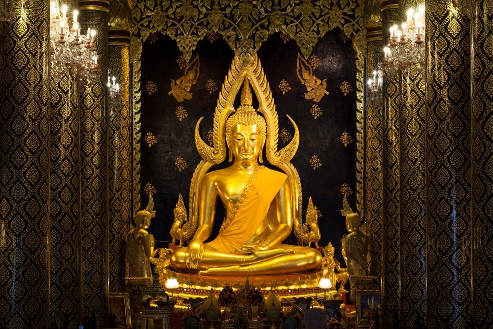 พระพุทธรูปทองคำขนาดใหญ่ตั้งอยู่ในศาลเจ้าที่ตกแต่งอย่างสวยงามพร้อม เที่ยวใกล้กรุงเทพ การแกะสลักที่ประณีตและรายละเอียดทองคำที่หรูหรา ทำให้เป็นสถานที่ท่องเที่ยวที่ต้องไปเยือนในสตูล โดยมีพระพุทธรูปขนาดเล็กสององค์ตั้งอยู่ทั้งสองข้าง.