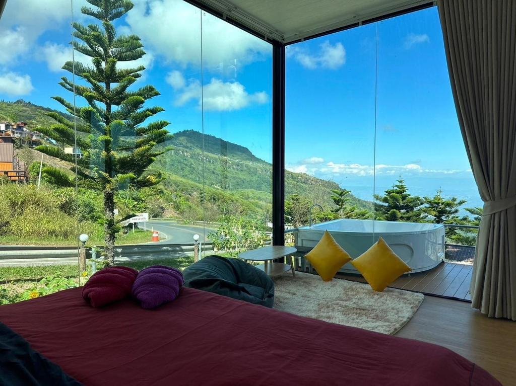 ห้องนอนที่มีผนังกระจกที่ ที่พักภูทับเบิก มองเห็นทิวทัศน์ภูเขา; อ่างอาบน้ำกลางแจ้งทรงกลมและโต๊ะเล็กตั้งอยู่บนระเบียงข้างหน้าต่างบานใหญ่.