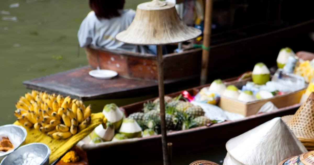ตลาดน้ำใกล้กรุงเทพ ที่มีชีวิตชีวา มีเรือแล่นไปมาบนผืนน้ำ ขายกล้วย สับปะรด มะพร้าว และสินค้าอื่นๆ ผู้คนบนเรือกำลังซื้อขายแลกเปลี่ยนกัน.