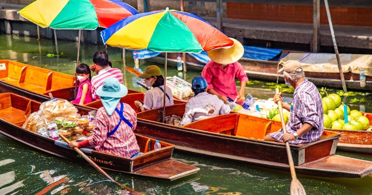 พ่อค้าแม่ค้าในเรือไม้ขายสินค้าและผลิตผลที่ตลาดน้ำ พร้อมร่มสีสันสดใสให้ร่มเงาใน ตลาดน้ำใกล้กรุงเทพ ที่คึกคักแห่งนี้.