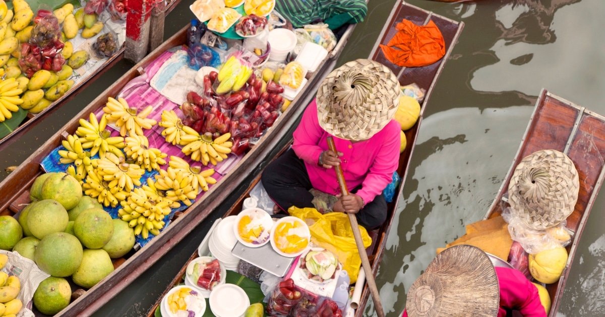 ภาพมุมสูงของพ่อค้าแม่ค้าในเรือไม้ขายผลไม้และอาหารที่ตลาดน้ำใกล้กรุงเทพฯ ( ตลาดน้ำใกล้กรุงเทพ ); พ่อค้าแม่ค้าสวมหมวกสานและเสื้อผ้าสีชมพู.