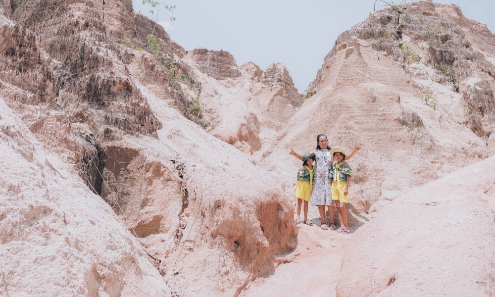 ผู้หญิงคนหนึ่งและเด็กสองคนในชุดสีเหลืองยืนอยู่บนทางเดินหินระหว่างหน้าผาสีอ่อนที่ ท่องเที่ยวสุราษฎร์ธานี ยอดนิยม ถ่ายทอดเสน่ห์ของสถานที่ท่องเที่ยวสุราษฎร์ธานีที่ไม่เหมือนใครแห่งนี้.